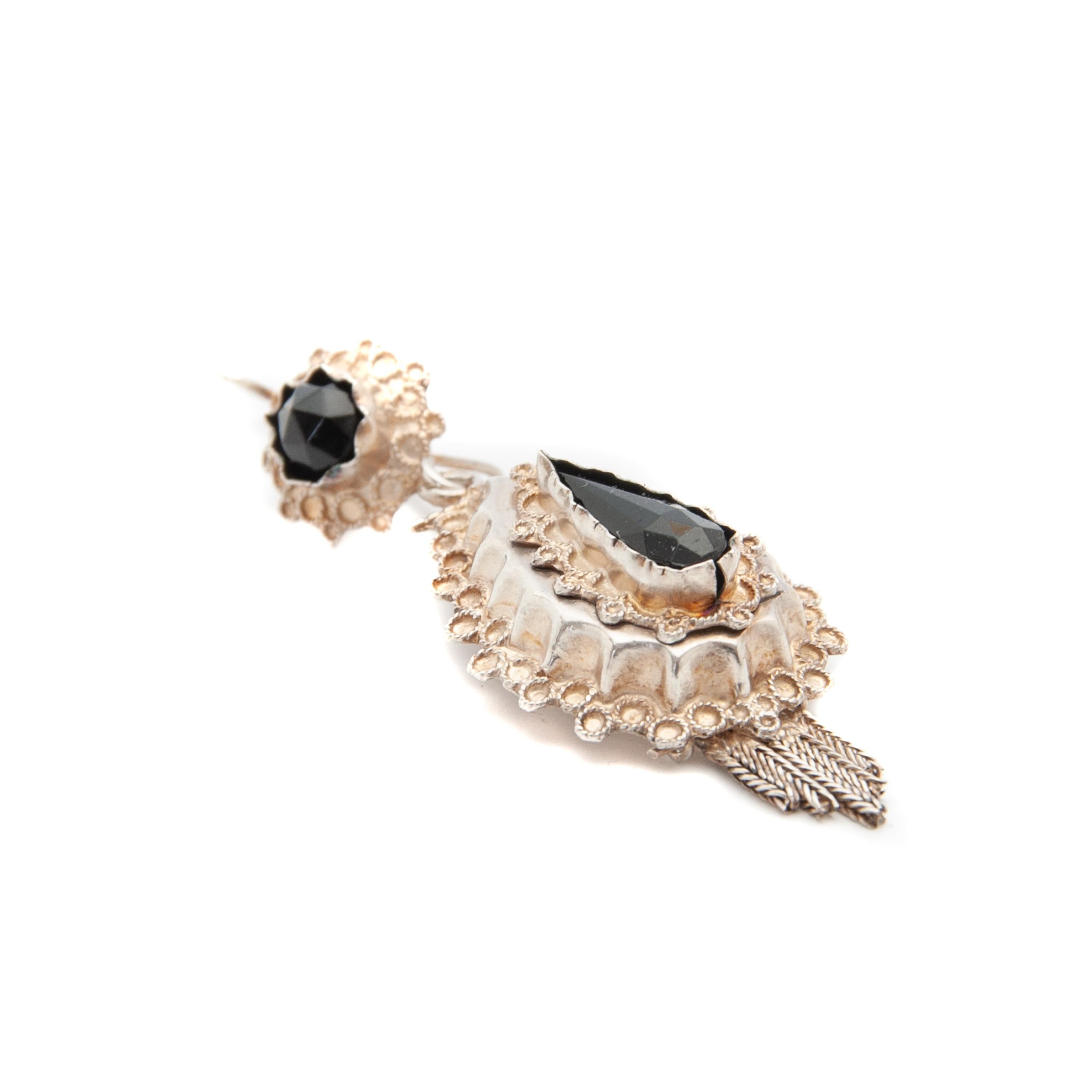 This earring was part of the regional dress in The Netherlands and made between 1906 and 1953. The design of the earring is made with fine silver filigree and set with black jet in bezel frame. The beautifully raised edge in its center piece has a
