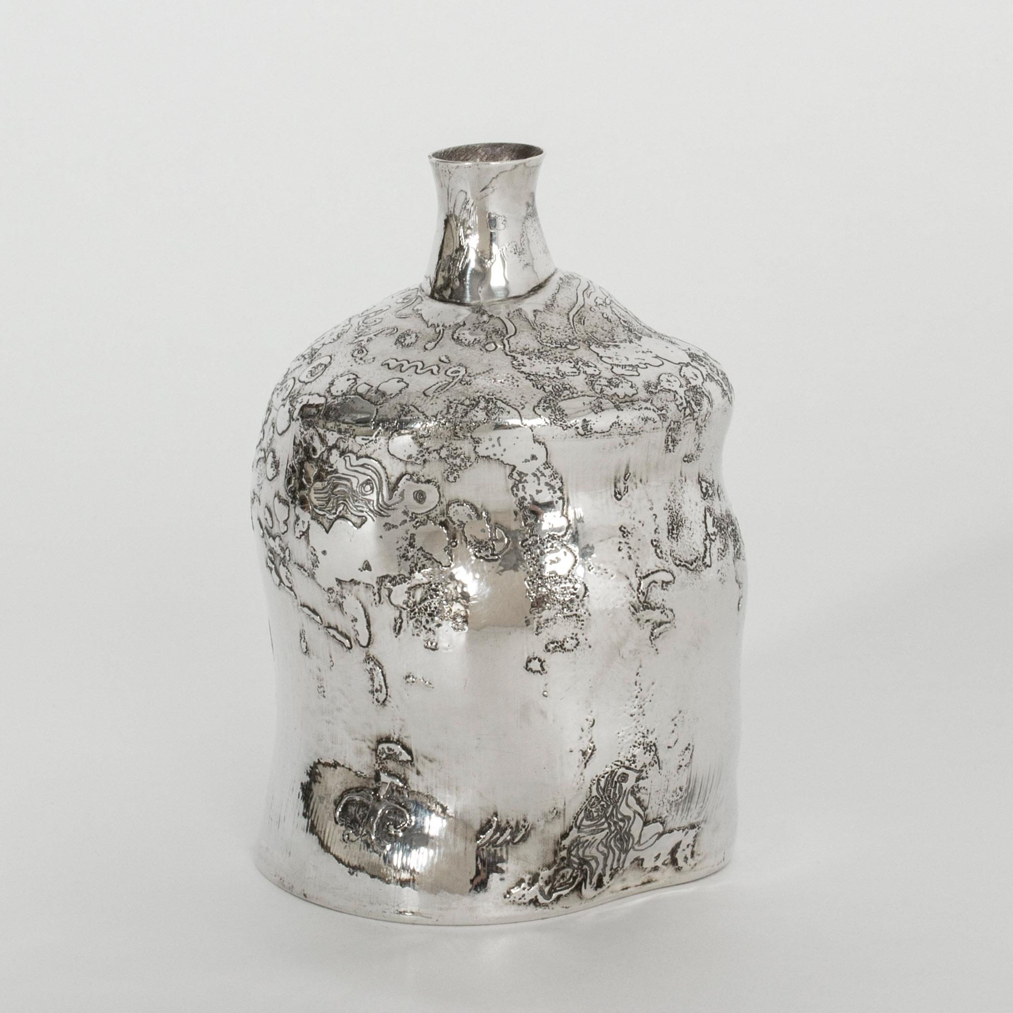 Amazing asymmetric silver bottle or vase by Olle Ohlsson with a flowing shape. The surface has been treated with acid to create an organic pattern, in which Ohlsson has etched faces, letters and lines. A piece with many beautiful, enigmatic details