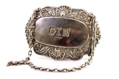 Silver bottle label with engraving and relief of the word Gin with chain