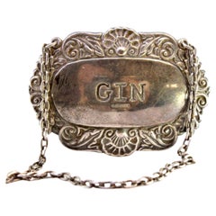Silver bottle label with engraving and relief of the word Gin with chain