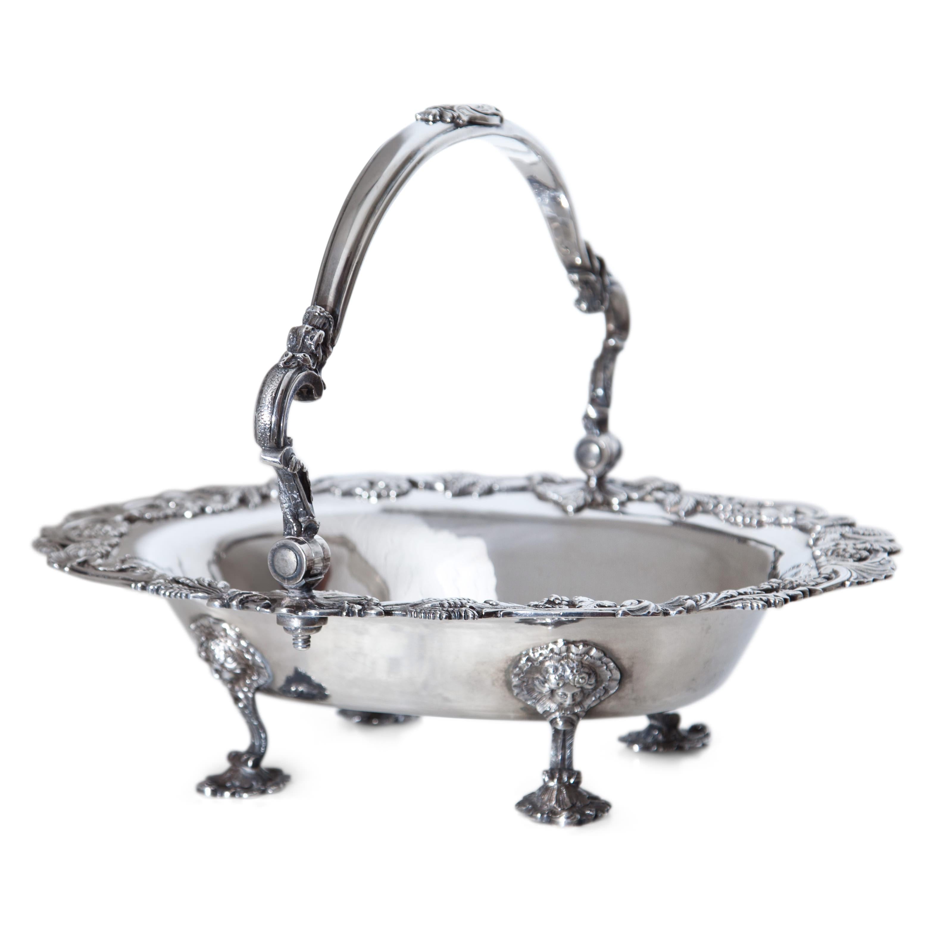 Silver bowl on high rocaille feet decorated with macarons and shells. The rim also shows decorations in the form of shells, ears of corn and vines. The smooth handle with asymmetrical rocaille ornamentation at the apex. On the mirror incised