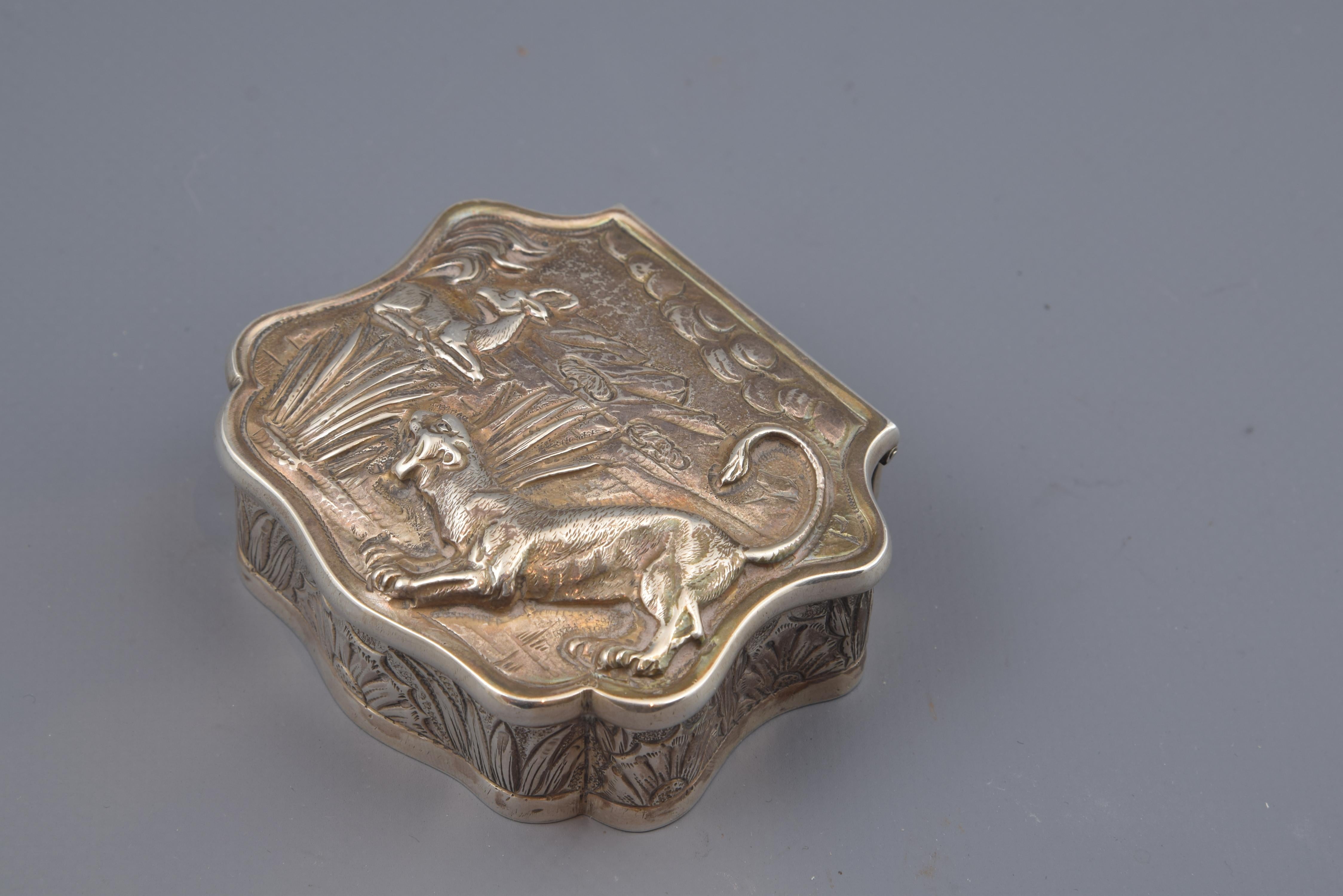 Box made of silver with flat lid and corrugated edges (except for the back, for the hinge), which has a decoration of plant elements on the edge flanked by a smooth molding to enhance them. The same is done at the top, highlighting a natural scene