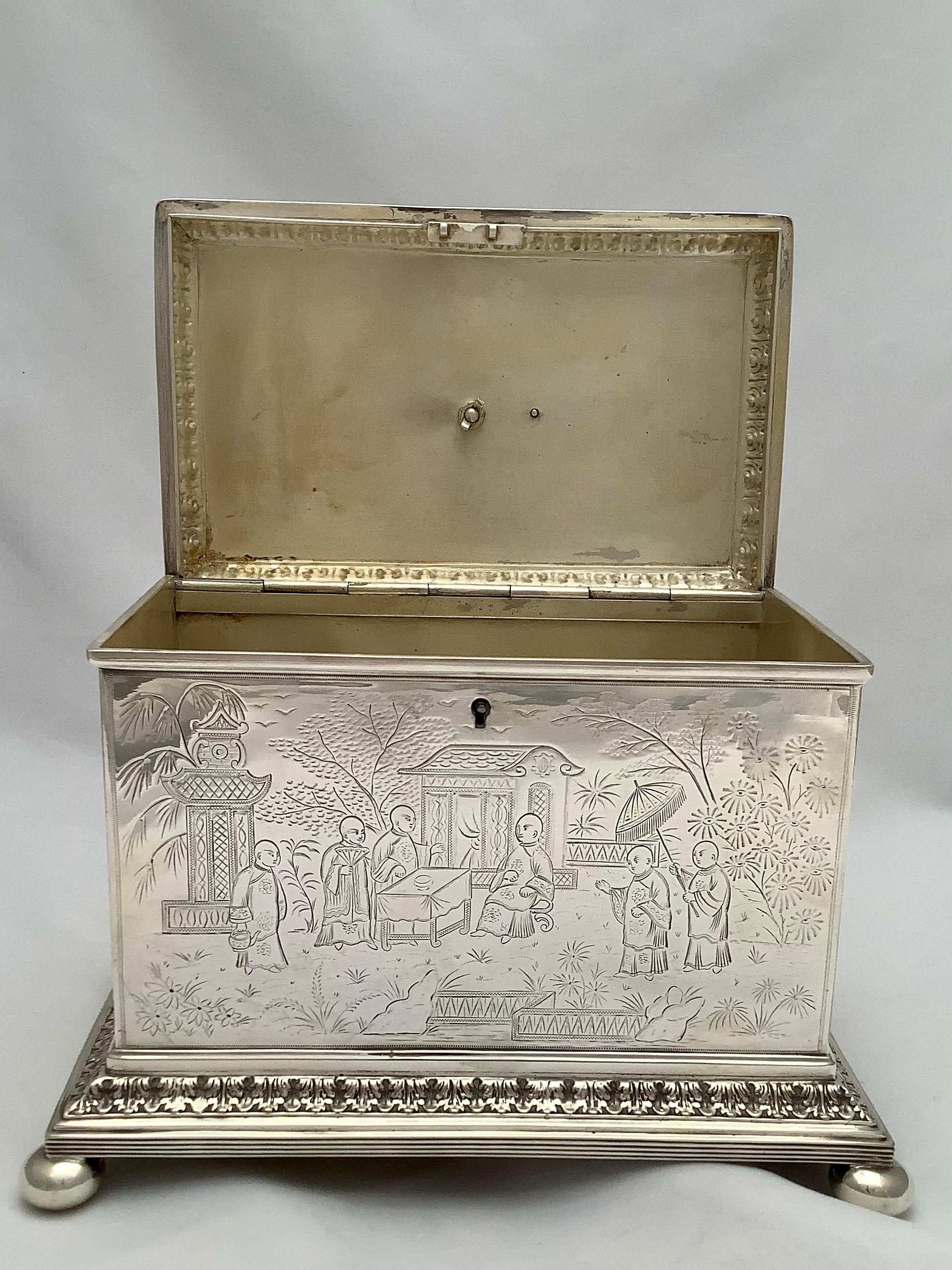 A silver tea caddy box with fine engraving depicting a Chinoiserie style design. Acanthus leaf details and sphinx sitting on top of the box. The box sits on four feet and has a locking mechanism as tea was a prized possession at the time the box was
