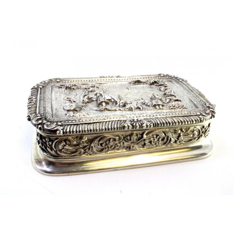 Description: Silver box with relief country motifs with houses in the background, surrounding frieze on the lid and garlands. Metal:. Origin: Portuguese. Mark: standing eagle. Weight: 481.69 grams. Dimensions: 12.5cmx7.7cm. Content: 833/1000. Assay