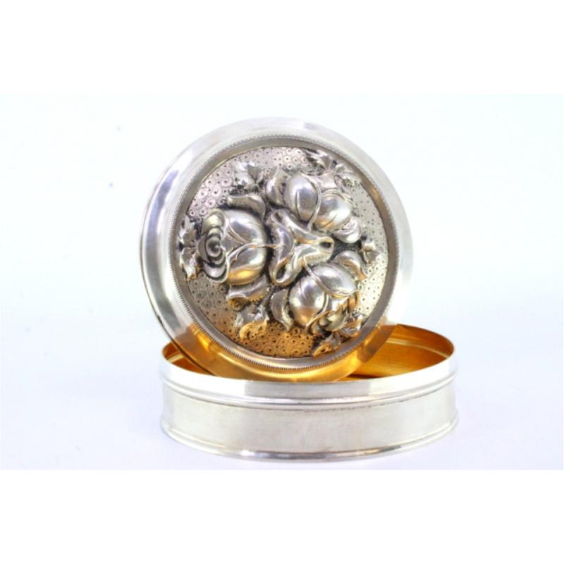 Description: Silver box with floral motifs in relief on the removable lid and gold interior. Metal: Silver. Origin: Portuguese. Mark: eagle on foot. Weight: 175.43 grams. Dimensions: 11.2cmx11.2cm. Content: 833/1000. Assay Mark: Yes, between 1938