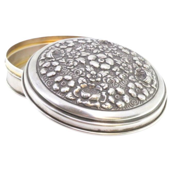 Silver box with embossed floral motifs on the removable lid and gold interior
