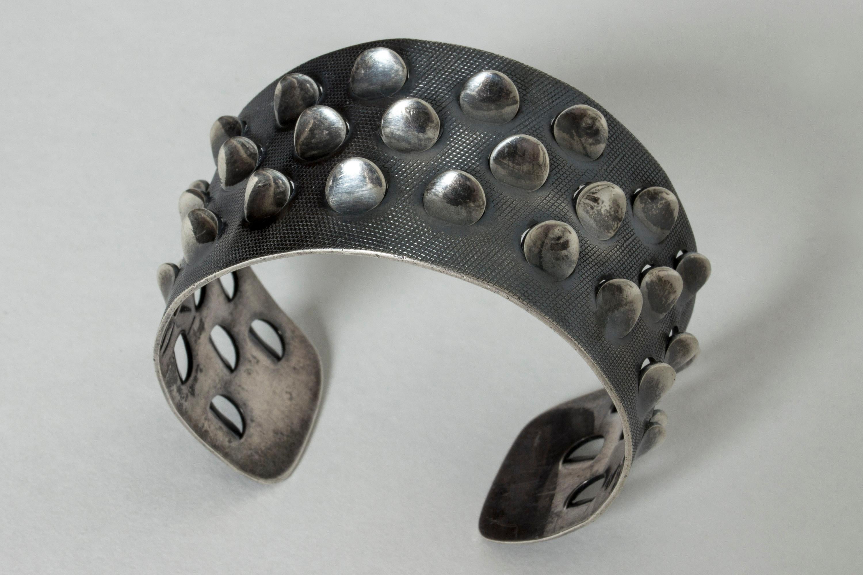 Stunning silver bracelet by Grete Prytz Kittelsen, in a cool, brutalist design with beautiful quality. The bracelet has an industrial pattern that serves as backdrop to the petallike flaps emerging from the surface. Wonderful play between hardcore