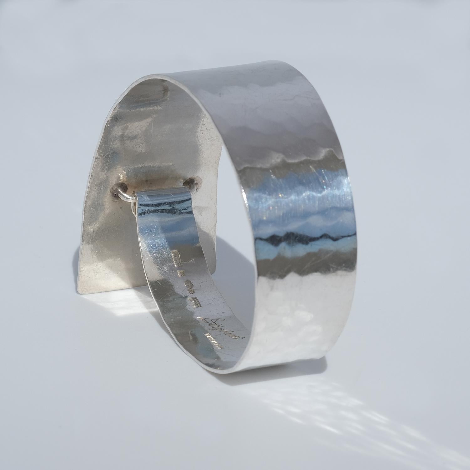 This fixed silver bangle has a beautiful hammered surface and it closes with a clip.

The endings of the bangle are of different sizes, making it resemble a beautiful modern geometric installation.