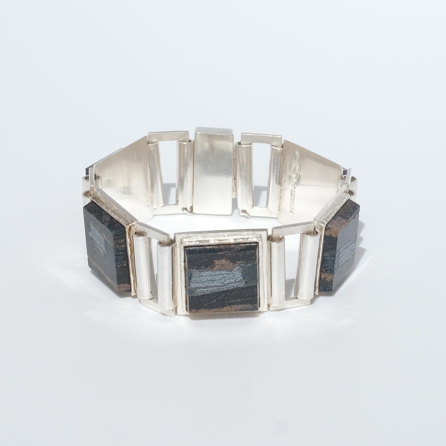 Dieses Armband ist aus Sterlingsilber und fünf quadratischen Schiefersteinen gefertigt. Die Schiefersteine sind durch silberne Rechtecke miteinander verbunden. Das Armband lässt sich leicht mit einem Kastenverschluss mit Sicherheitskette schließen.