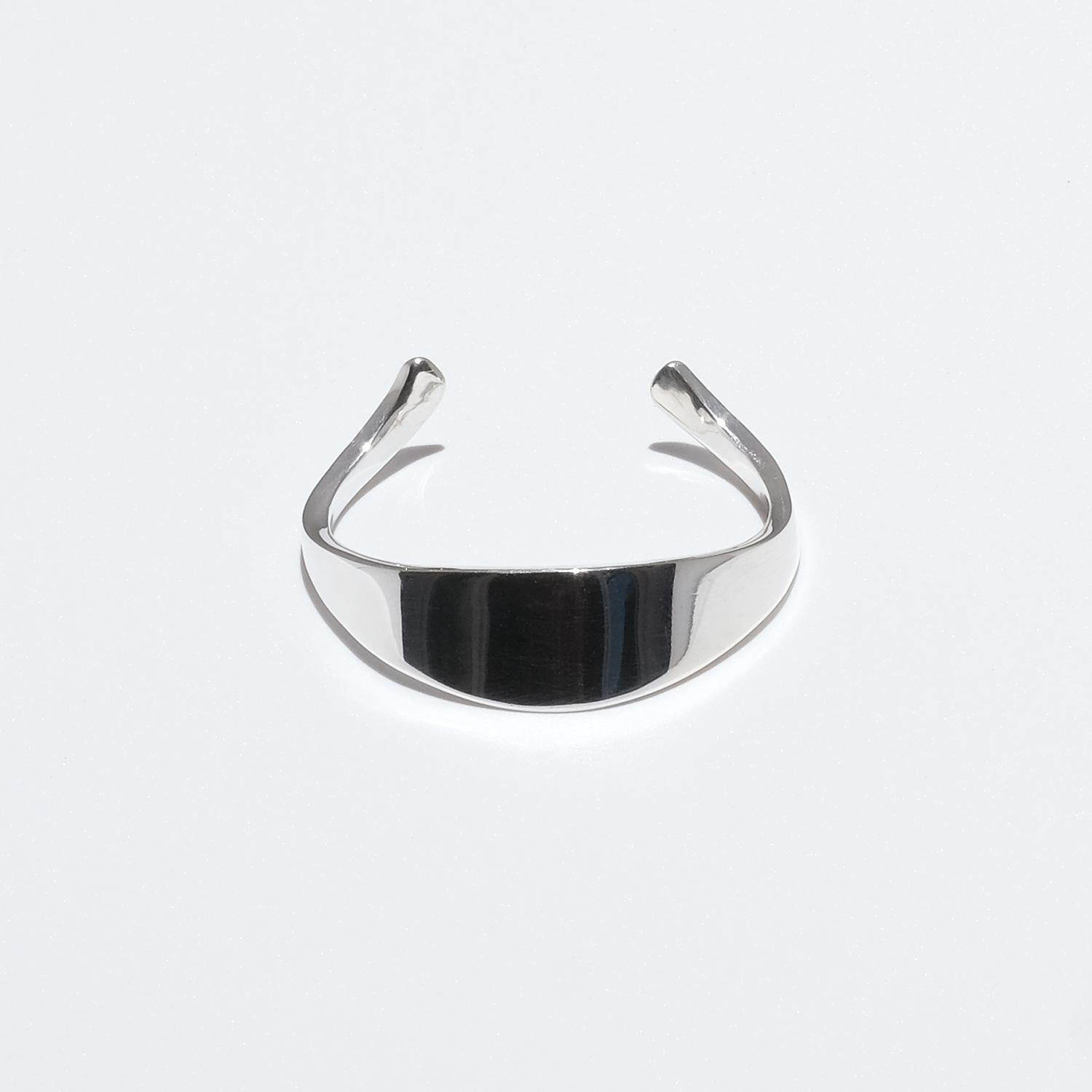 This sterling silver cuff bracelet has a glossy surface. Its shape resembles a napkin-ring with two beautifully bent arms. Its upper part runs in a straight as well as in an arciform line giving the bracelet its unique shape.

This bracelet may not