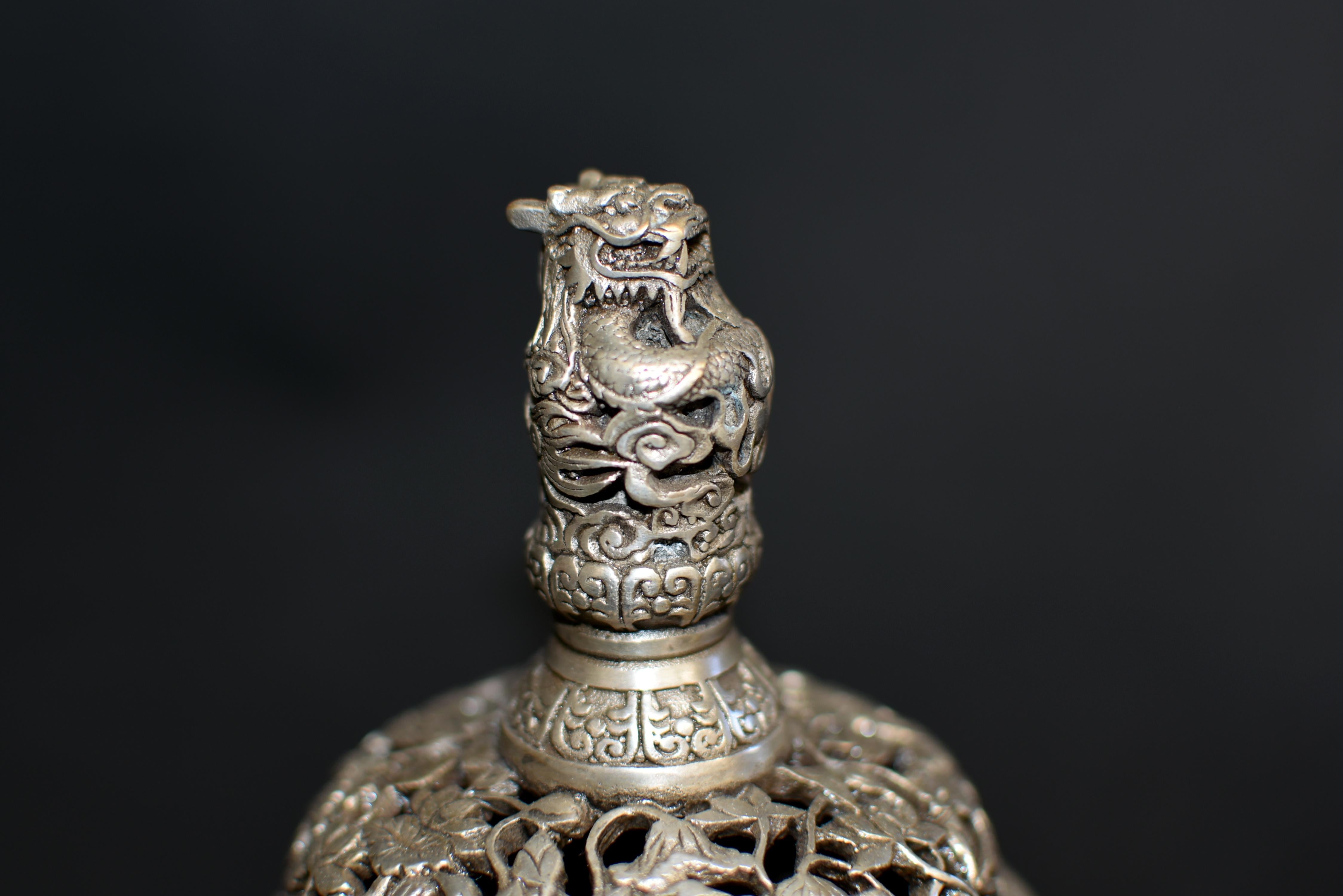 The finely made, silver bronze, round-form censer is raised on three egrets standing on a lotus leaf. The body is extensively embossed with scrolls of leaves amid blooming peonies, flanked by a pair of dragons looking in opposite directions with