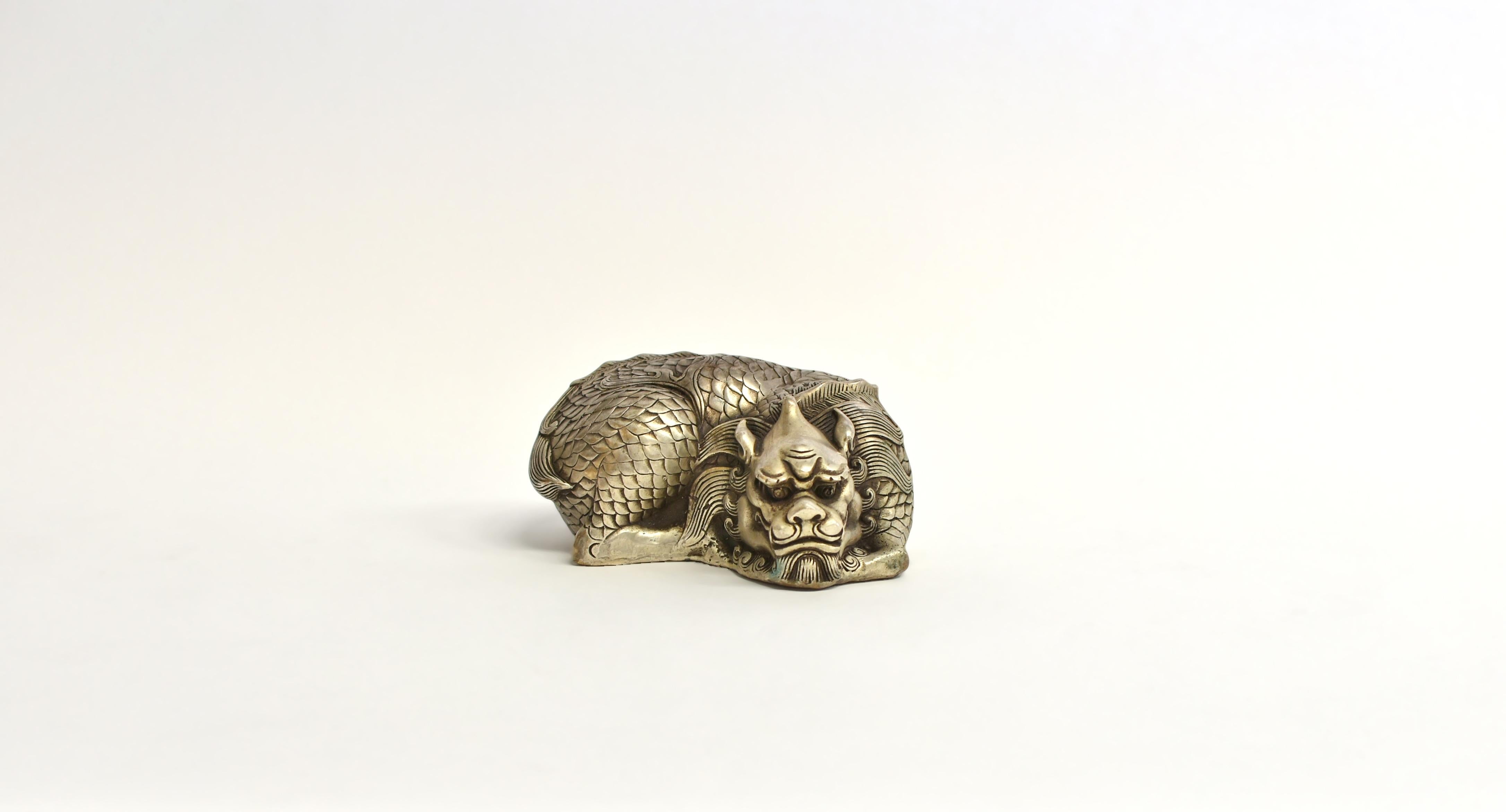A most unique coiled silver bronze dragon statue. Contrary to the common ferocious form, this dragon appears to be calm and genial. The head rests on arms just above the ground with back-swept whiskers. Its talons are nearly invisible tucked under