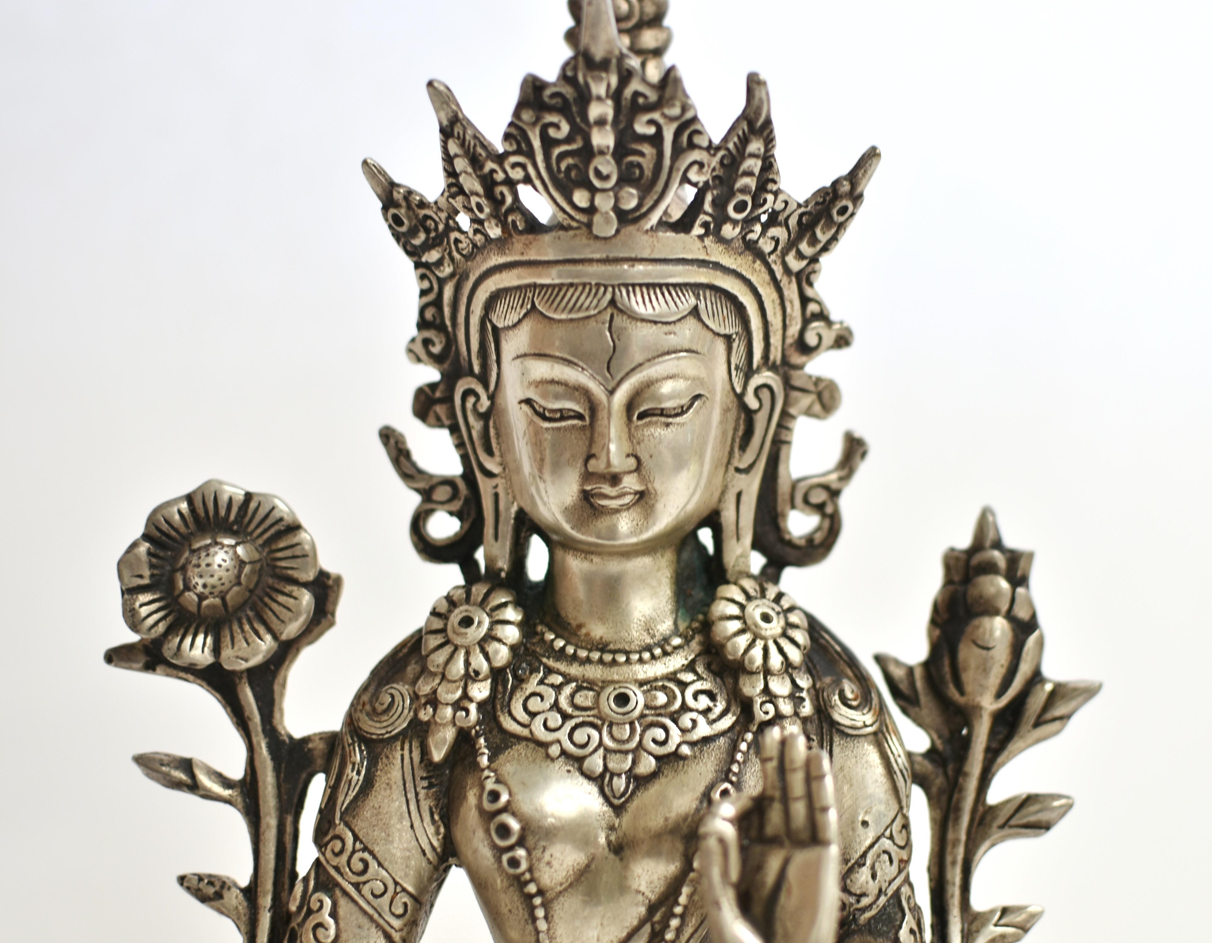 A beautiful silver bronze White Tara statue. The serene face with large downcast eyes under arched eyebrows above pursed lips, flanked by long earlobes, all under hair neatly tied and adorned with an elaborate crown. Extra eyes between the brows, on