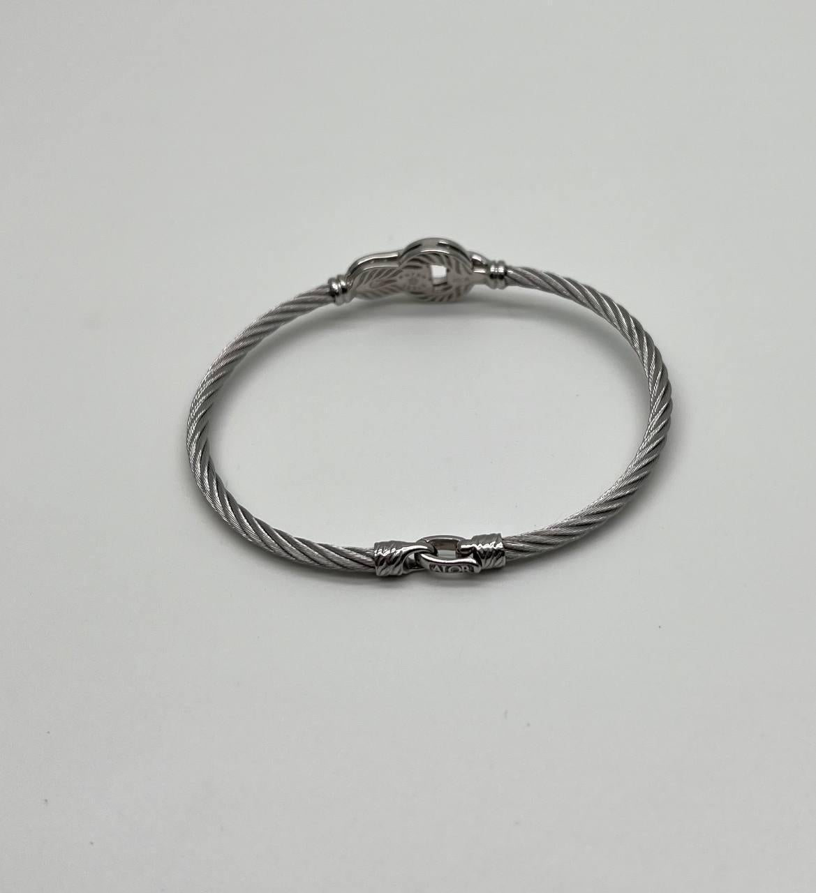 Confectionné avec un câble en argent torsadé, il présente un motif central en or blanc 18 carats orné de diamants étincelants. Finement construit en métal d'acier poli. Une pièce qui incarne la sophistication et le style. 0,20 ctw Diamants de