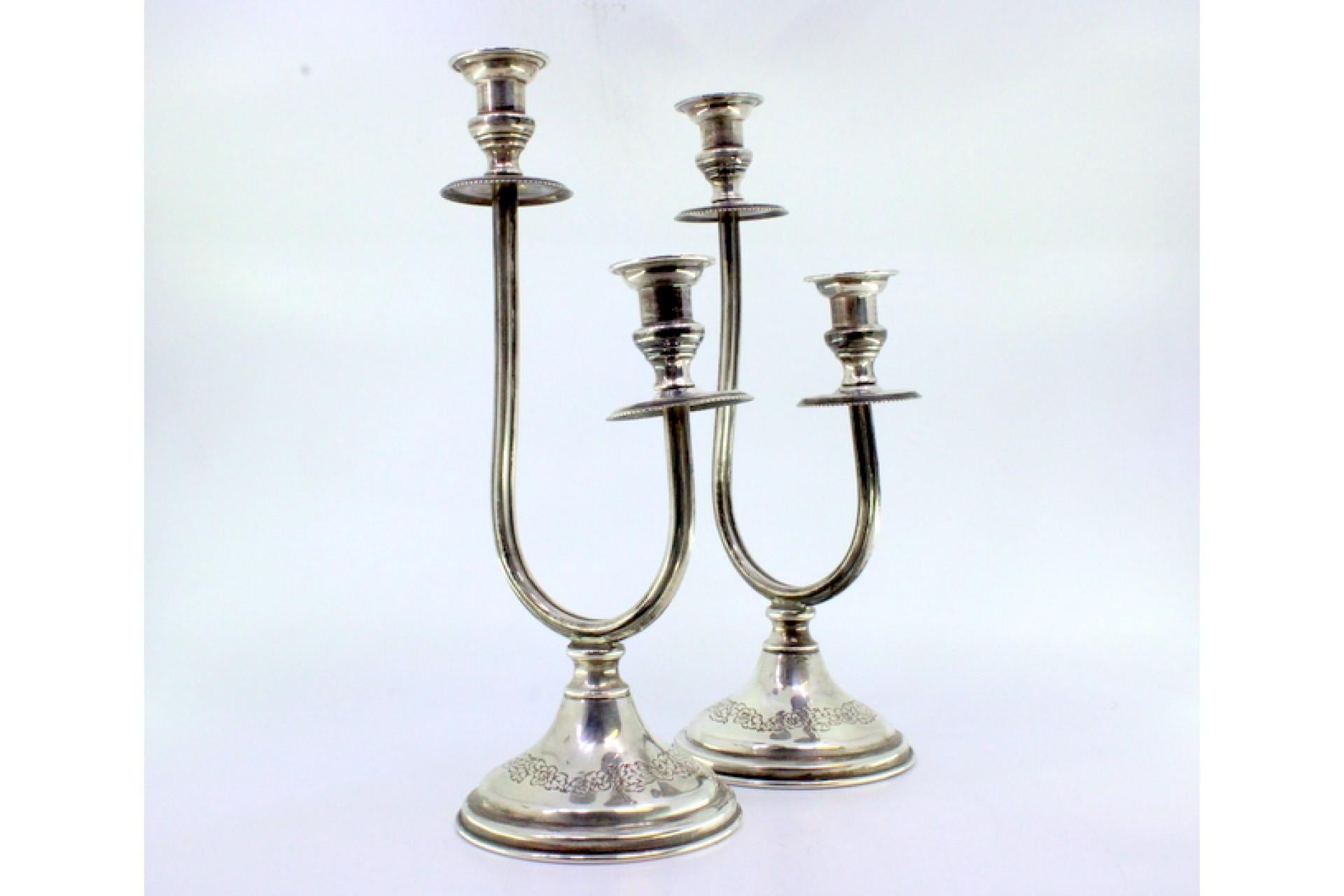 Description: Two-light silver candelabra with floral reliefs on the circular bases. Metal: Silver. Origin: Portuguese. Mark: Open-winged eagle. Weight: 355.41 grams. Dimensions: 26.8cm x 10cm. Content: 835/1000. Assay Mark: Yes, between 1938 and