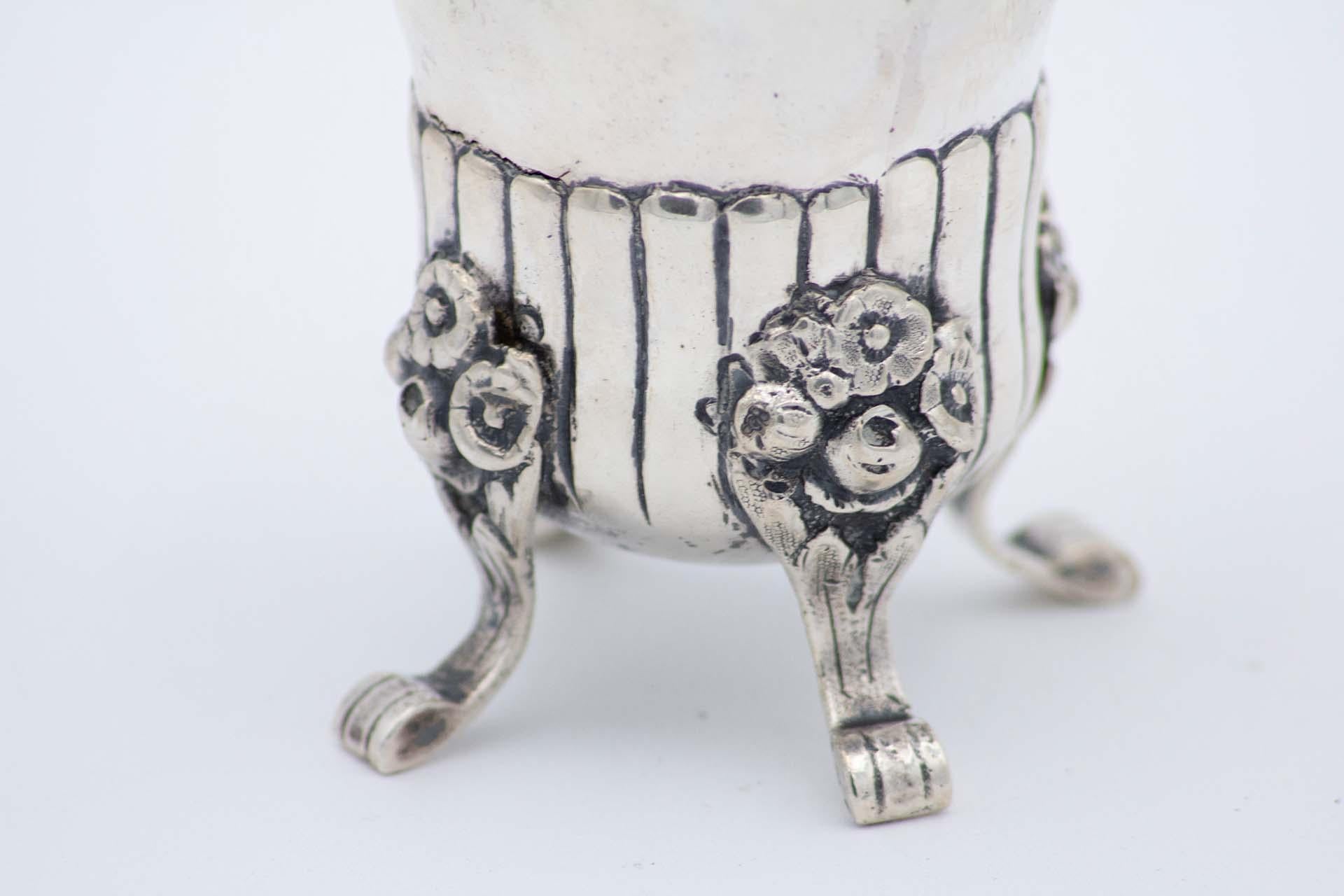 Description: Silver candlestick with floral motifs, raised sections and bows, and resting on four raised, engraved feet. Metal: Silver. Origin: Swedish. Brand: Trevo. Weight: 264.64 grams. Dimensions: 7.7cmx18.7cm. Content: 835. Assay Mark: Yes,