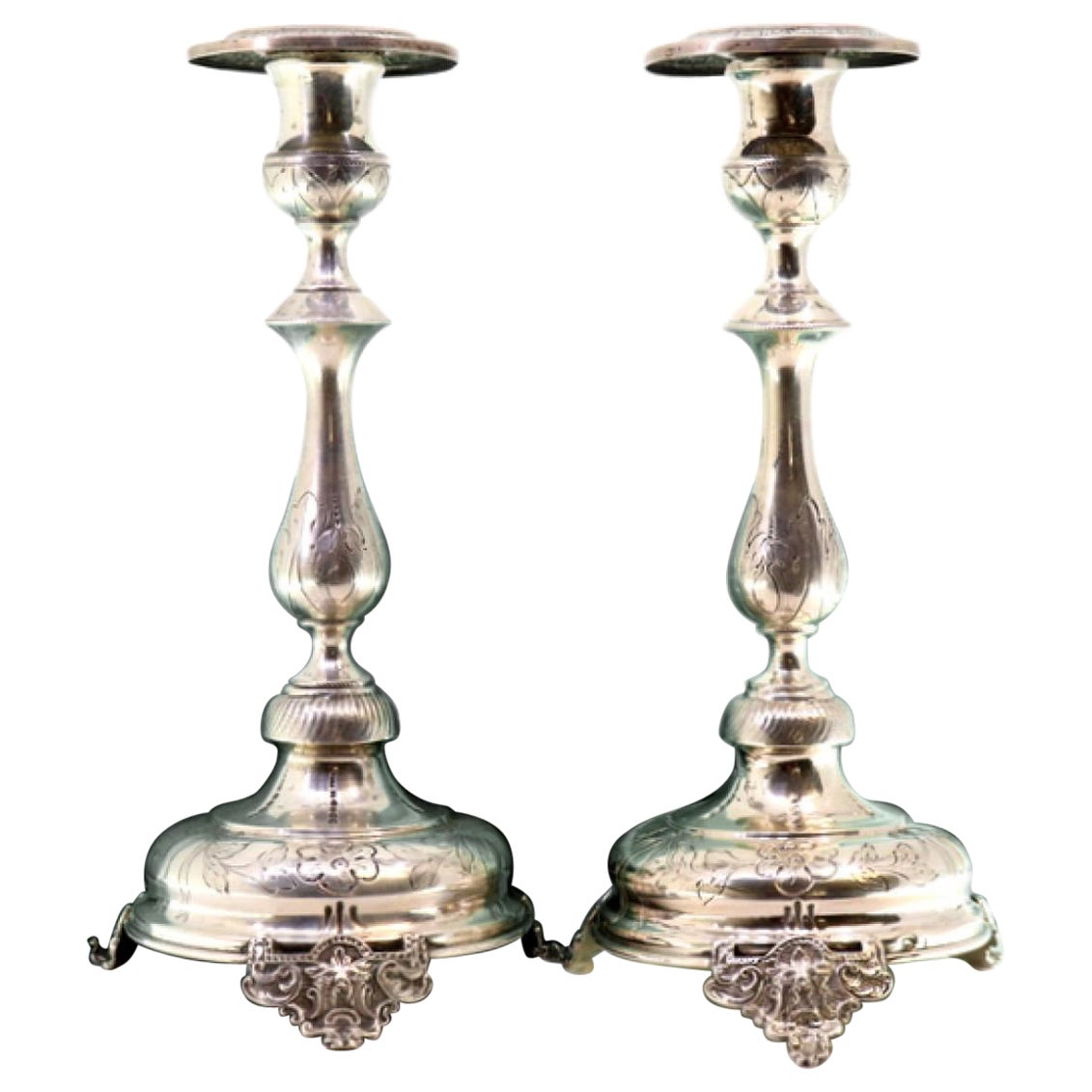 Silver candlesticks with floral engravings on circular bases with three feet