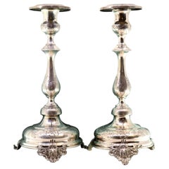 Silver candlesticks with floral engravings on circular bases with three feet