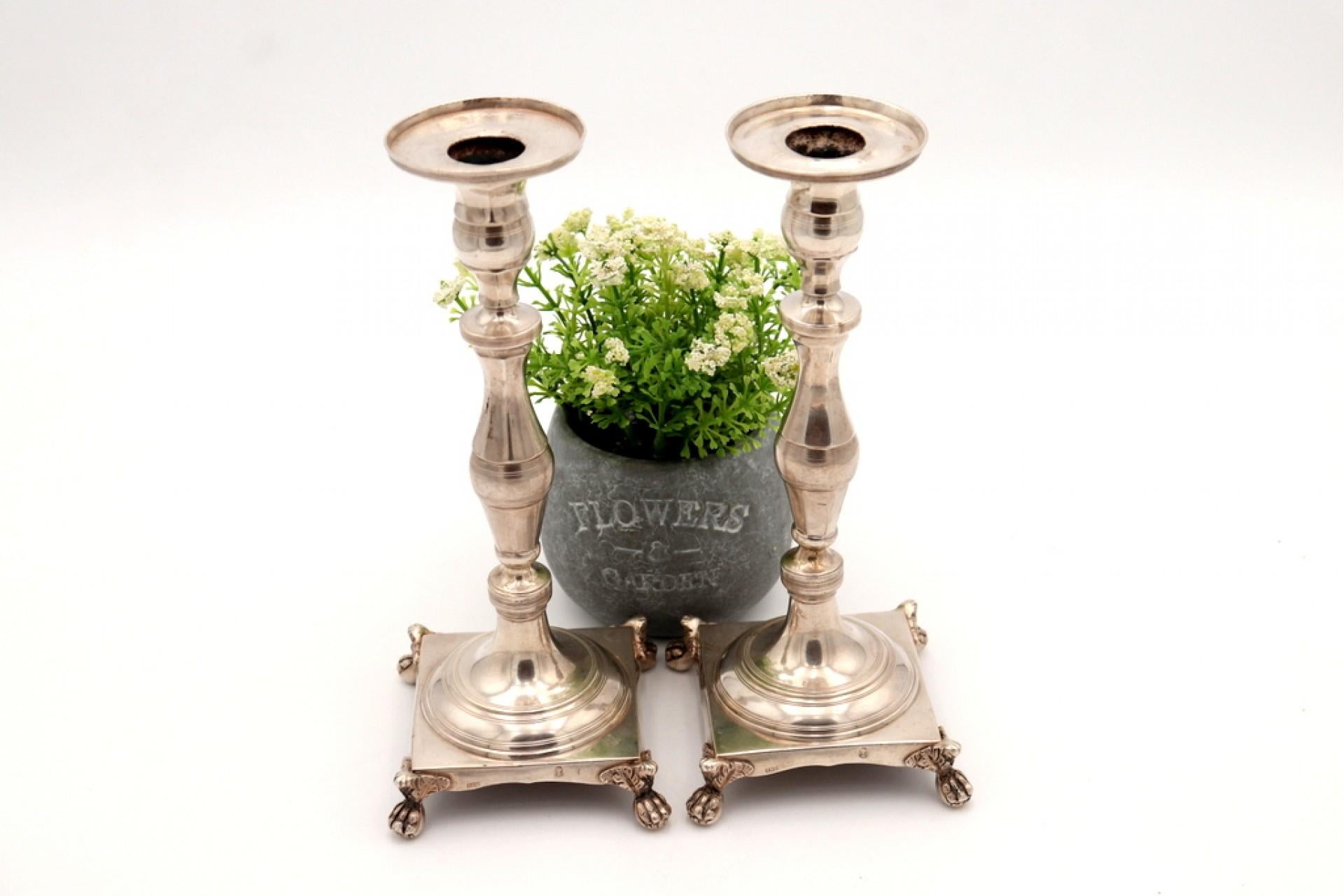 Description: Silver candlesticks with turned shafts resting on square bases with four claw-shaped feet. Metal: Silver. Origin: Portuguese. Brand: Lisbon Crown. Weight: 741.98 grams. Dimensions: 9.5cmx23cm. Content: 833/1000. Assay Mark: Yes, from