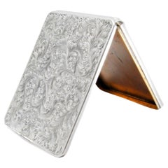 Caja de cartón plateada con diseños grabados, tapa abatible e interior dorado