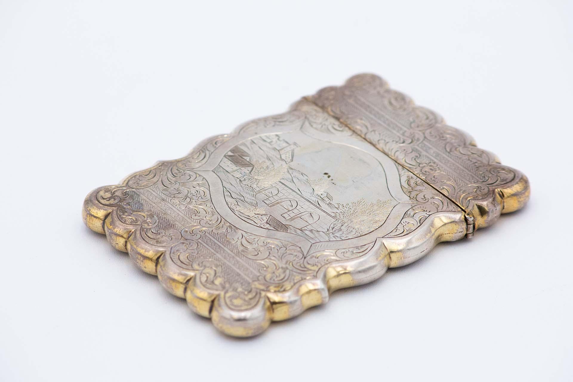 Description: Silver card case with guilloche engravings featuring a countryside landscape, bands at the top, garlands and wavy border. Metal: Silver. Origin: Portuguese. Brand: IR. Weight: 125.97 grams. Dimensions: 10.8cmx0.9cm. Content: 833/1000.