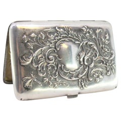 Silver case with embossed florals around monogram and hinged lid