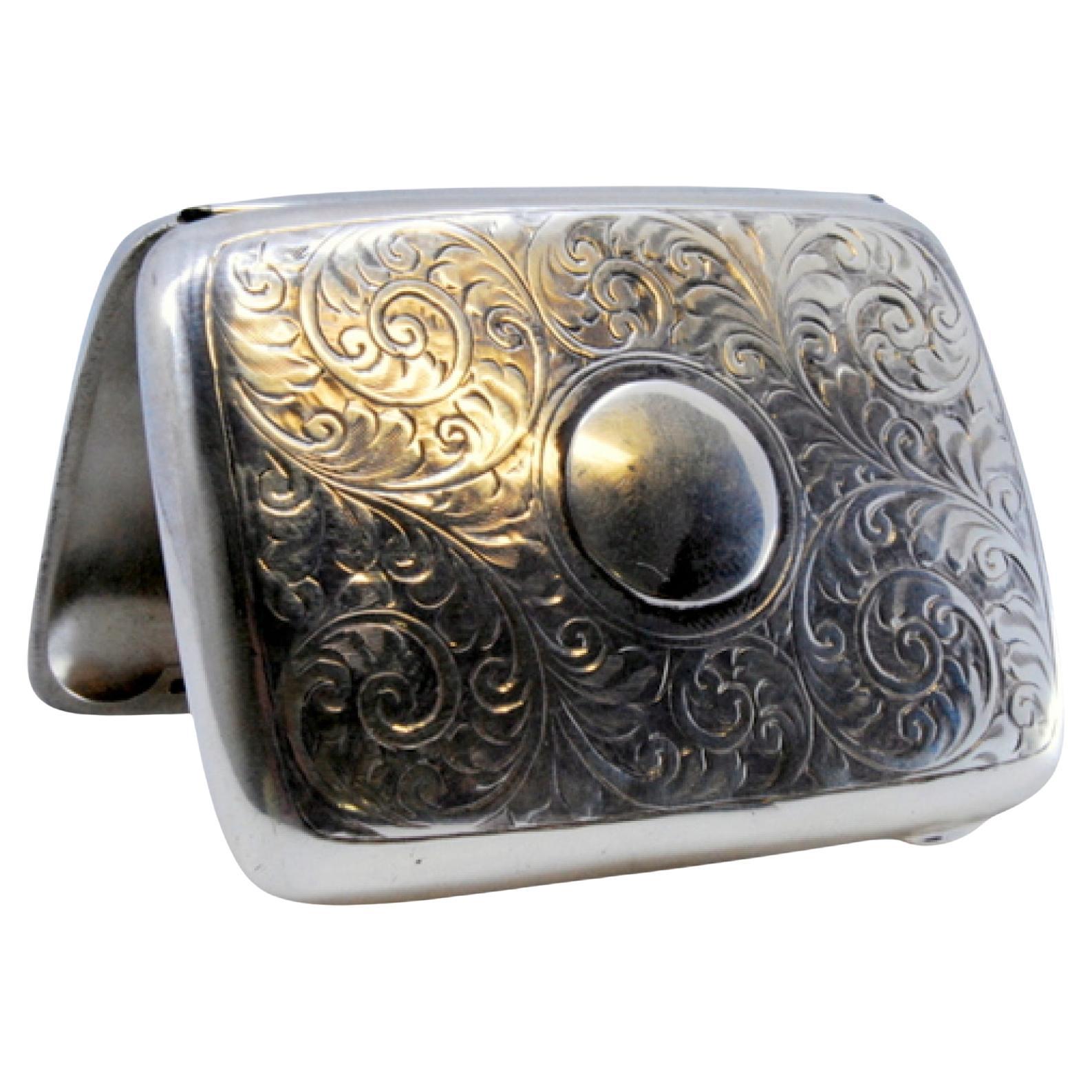 Silver case with floral engravings around curved monogram and hinged lid