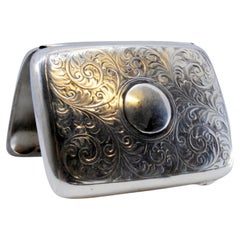Silver case with floral engravings around curved monogram and hinged lid