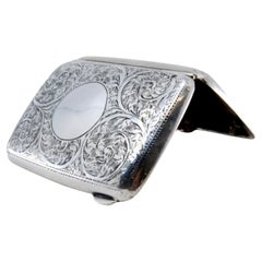 Silver case with floral engravings around curved monogram and hinged lid