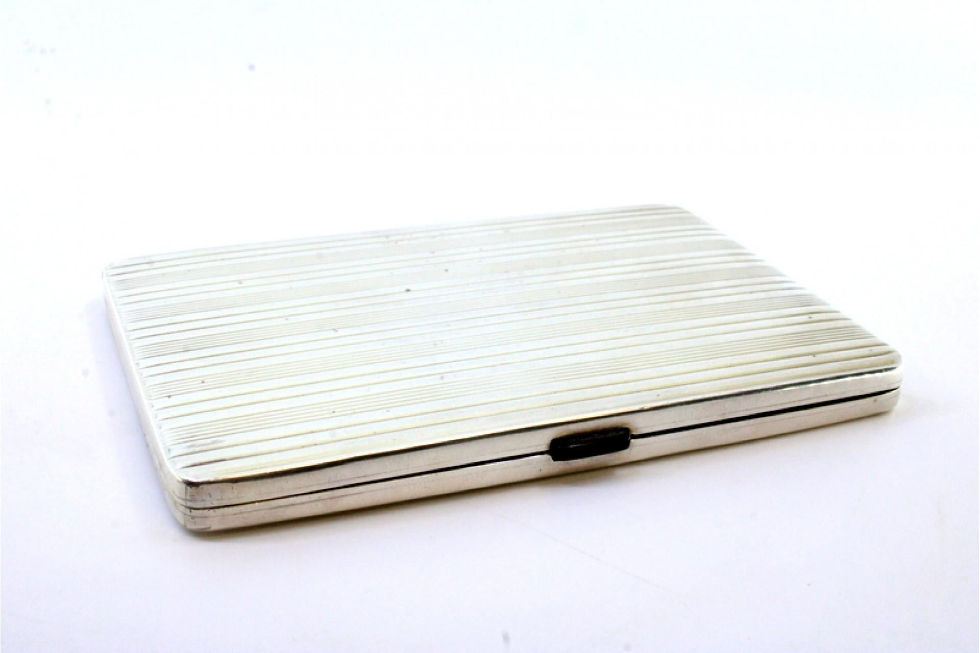 Description: Silver cigarette case with fluted stripes at the top, gold interior, cigarette holder with tilting spring. Metal: Silver. Origin: Hungarian. Brand: Eagle Head. Weight: 223.75 grams. Dimensions: 12cmx8cm. Content: 900/1000. Assay Mark: