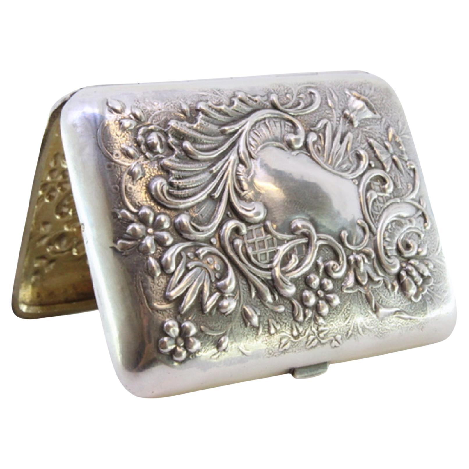 Silver case with raised reliefs and interior monogram in gold with ribbon