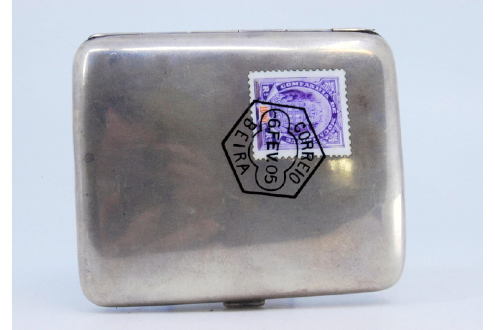 Description: Silver cigarette case with smooth lid and enamel seal with Mozambique postmark, hinged lid. Metal: Silver. Origin: European. Mark: Absent. Weight: 120.36 grams. Dimensions: 8.8x7.2cm. Content: 833/1000. Assay Mark: Absent. Additional