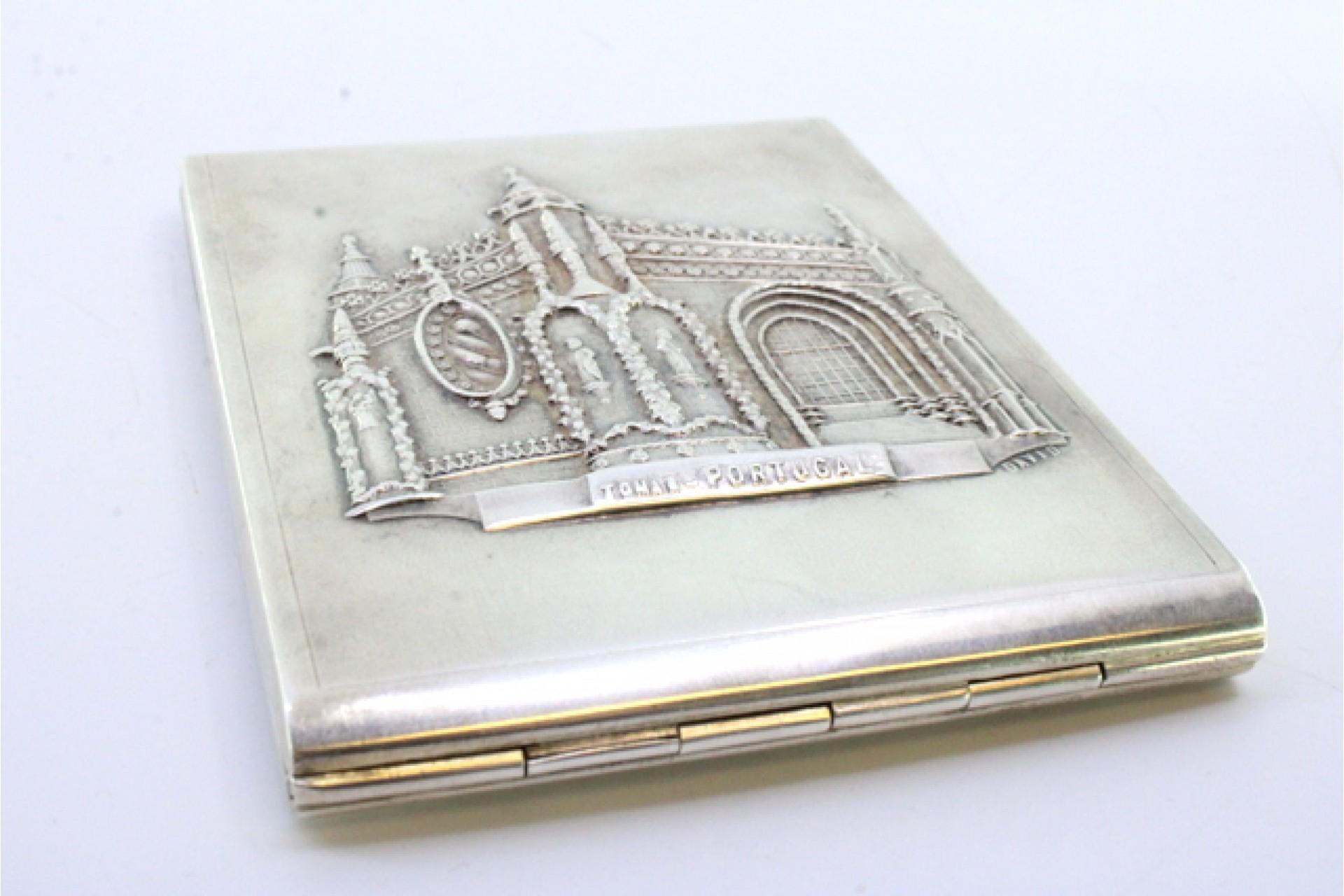 Description: Silver cigarette case with reliefs alluding to the Convent of Tomar on the hinged lid and gold interior. Metal: Silver. Origin: Portuguese. Mark: Cabeça de escravo. Weight: 127.51 grams. Dimensions: 10.5cmx8cm. Content: 833/1000. Assay