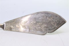 Silver cheese knife with floral engravings and reed-style embossed handle
