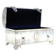 Boîte à bijoux en argent en forme de coffre avec applications de pièces de monnaie, velours bleu et pieds découpés.