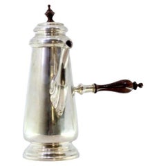 Silver chocolate maker with wooden handle and placed on a round base