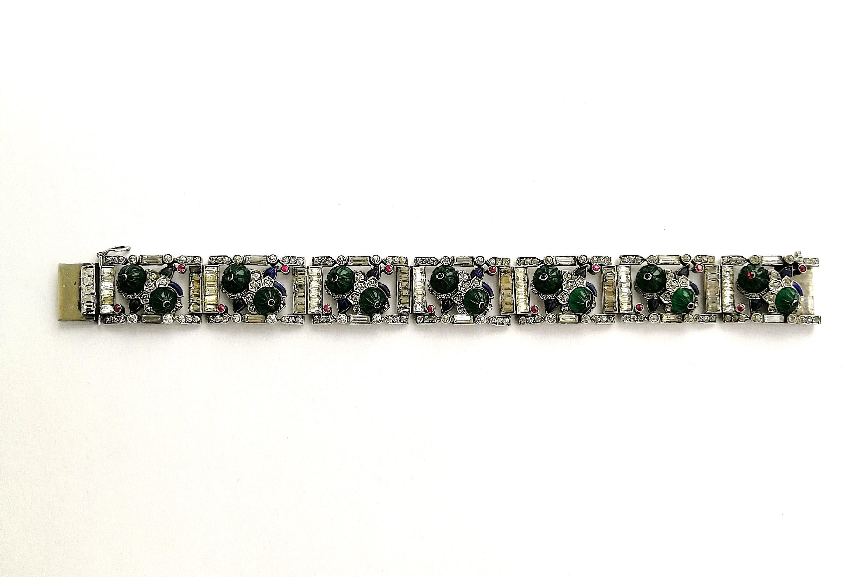 An exquisite and rare bracelet from the 1920s, in high Cartier style. Hand set melon cut emerald paste cabuchons, highlighted with a single ruby paste, and sapphire and emerald pastes are set, alongside clear round and baguette pastes in sterling