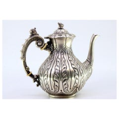 Silver coffee pot with raised engraving and a dragon-shaped handle on the lid