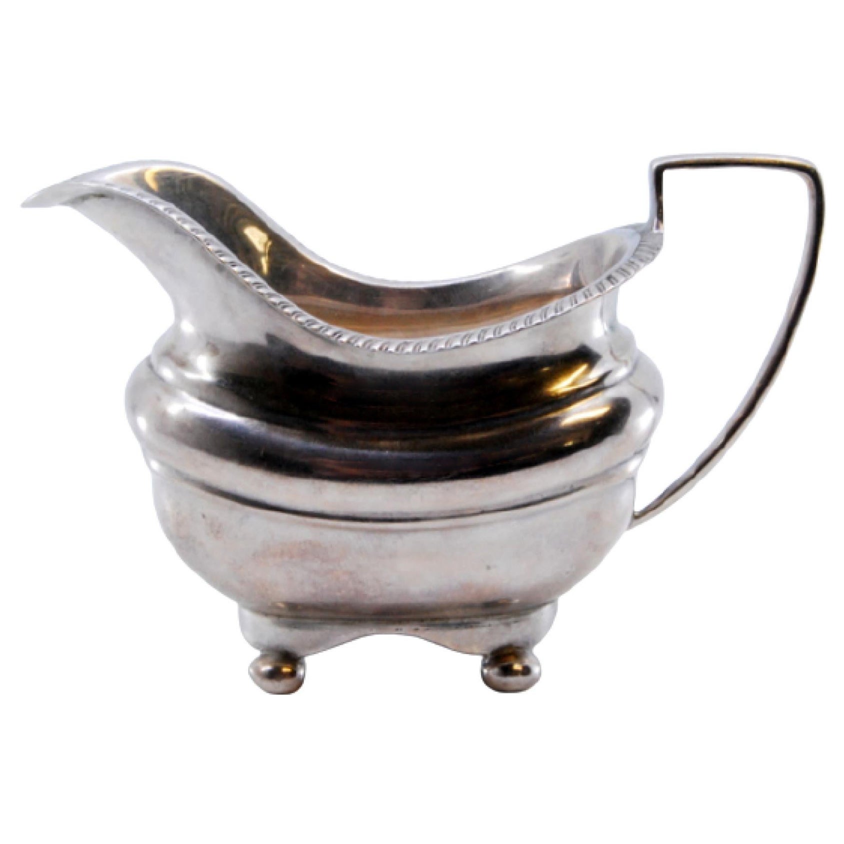 Silver creamer with a beaded edge and resting on four round feet