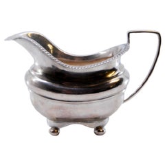 Silver creamer with a beaded edge and resting on four round feet