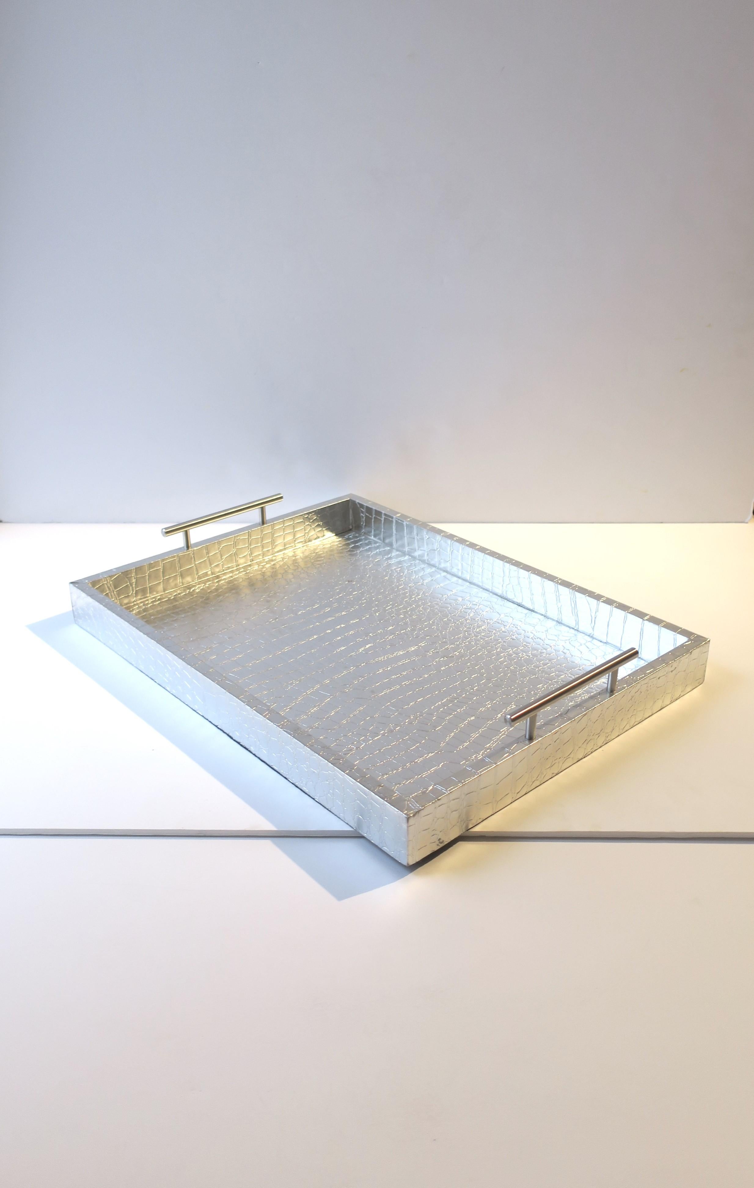 A silver faux crocodile or alligator serving or storage tray with metal handles. This rectangular tray is wrapped in a silver faux crocodile or alligator material and finished with brushed chrome metal handles. Tray is great for serving or to