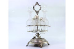 Silver cruet set with polished vessels and three-footed base with masks