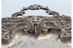 Silver crumb catcher w/ mask, shells & central floral engravings