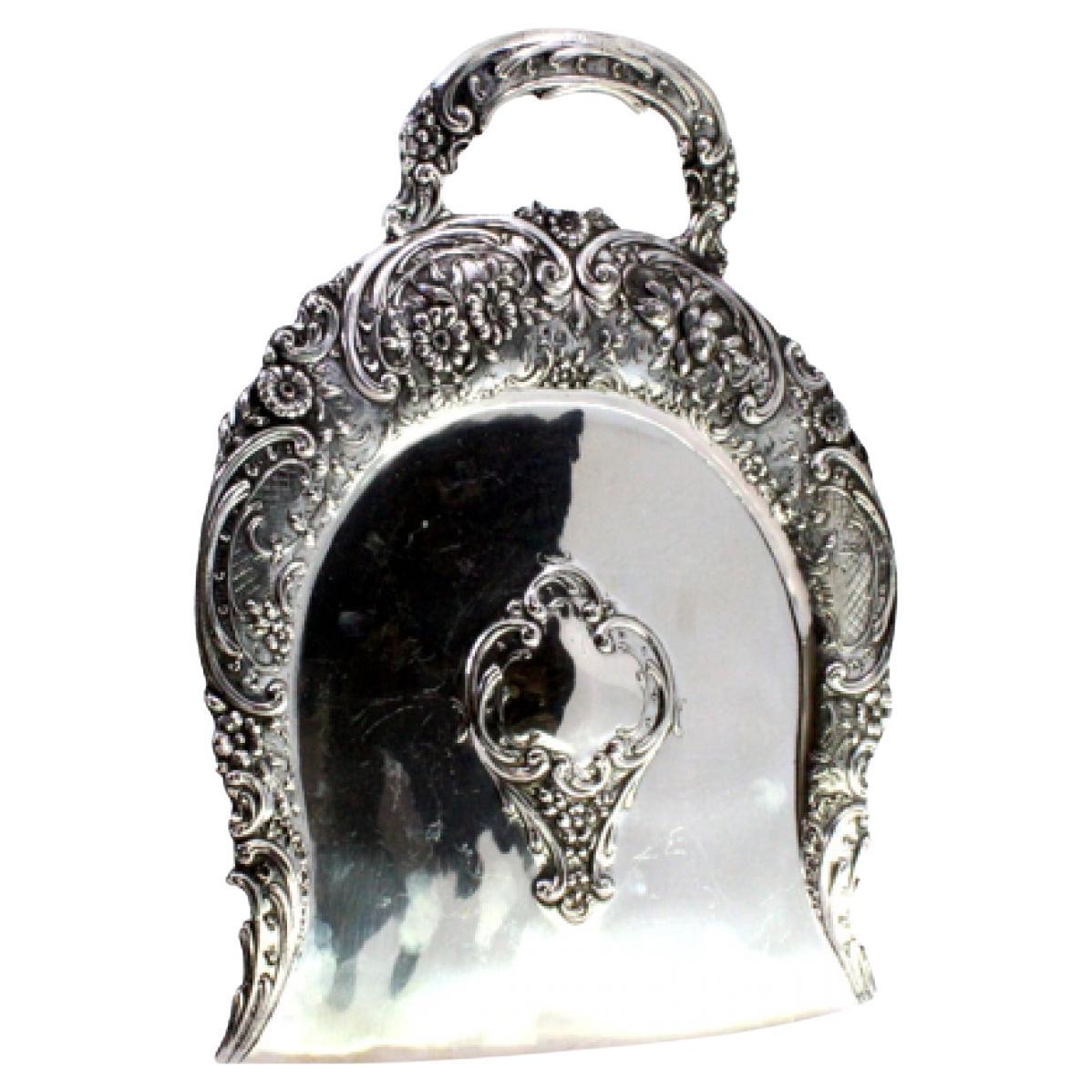 Silberner Krümelfänger mit enthüllten floralen Motiven, die eine Monogramm-Karte umgeben