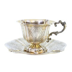 Silver cup and saucer with engraved floral motifs and cutouts on the edges