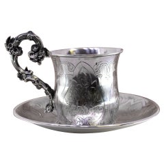 Silver cup and saucer with floral engravings and raised handle details