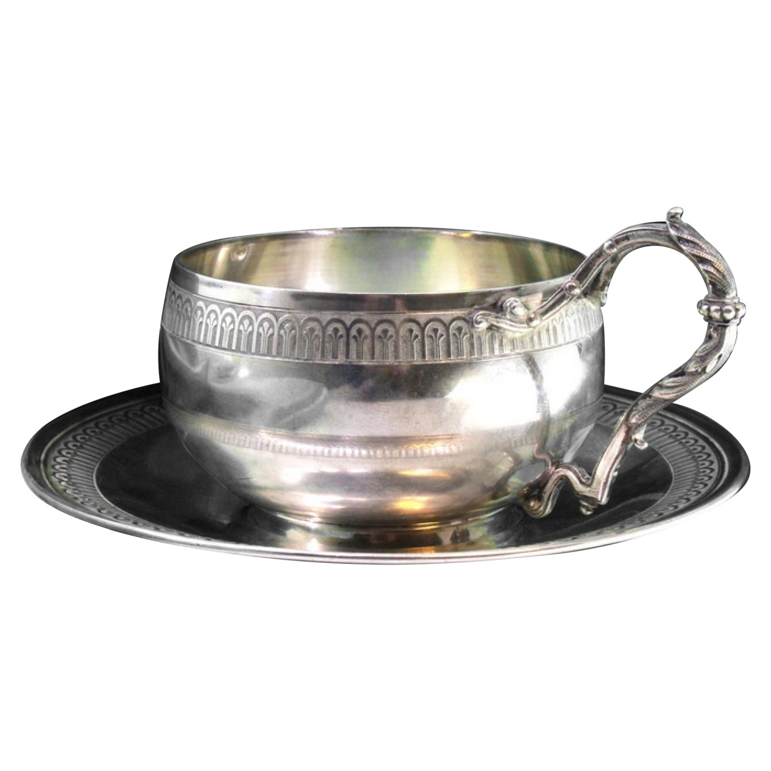 Silver cup and saucer with raised friezes on the edge and cut-out handle