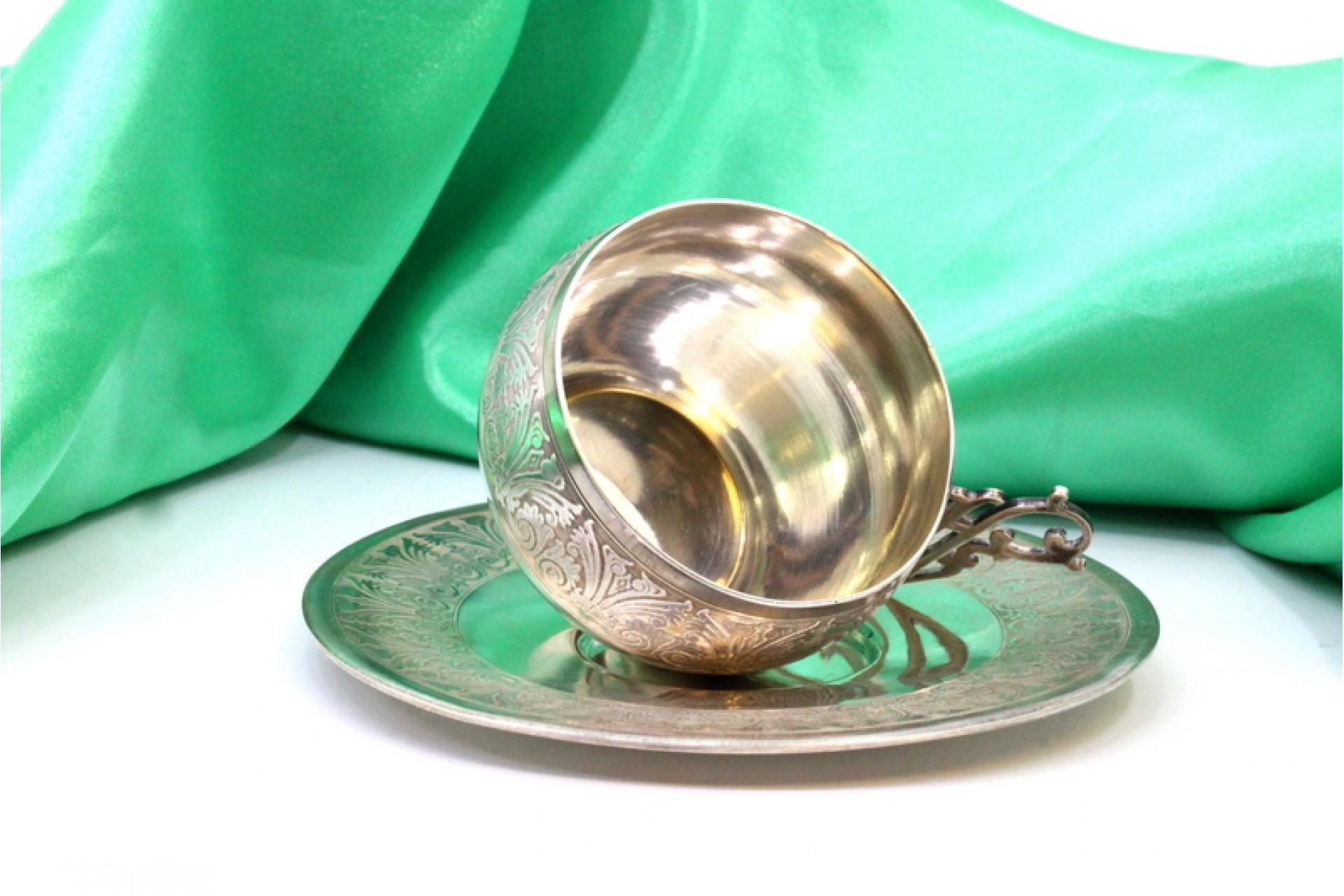 Beschreibung: Silberne Tasse und Untertasse mit Reliefs und Applikationen mit Ausschnitten an den Henkeln. Metall: Silber. Herkunft: Französisch. Marke: Tête Minerve. Gewicht: 107,48 Gramm. Abmessungen: Untertasse - 12x12cm Tasse - 6x5,5cm. Inhalt: