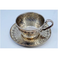 Silver cup and saucer with wavy engravings and friezes around the edges