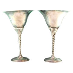 Silver cups w/ high stems 
twists on circular bases w/ engraved plant motifs